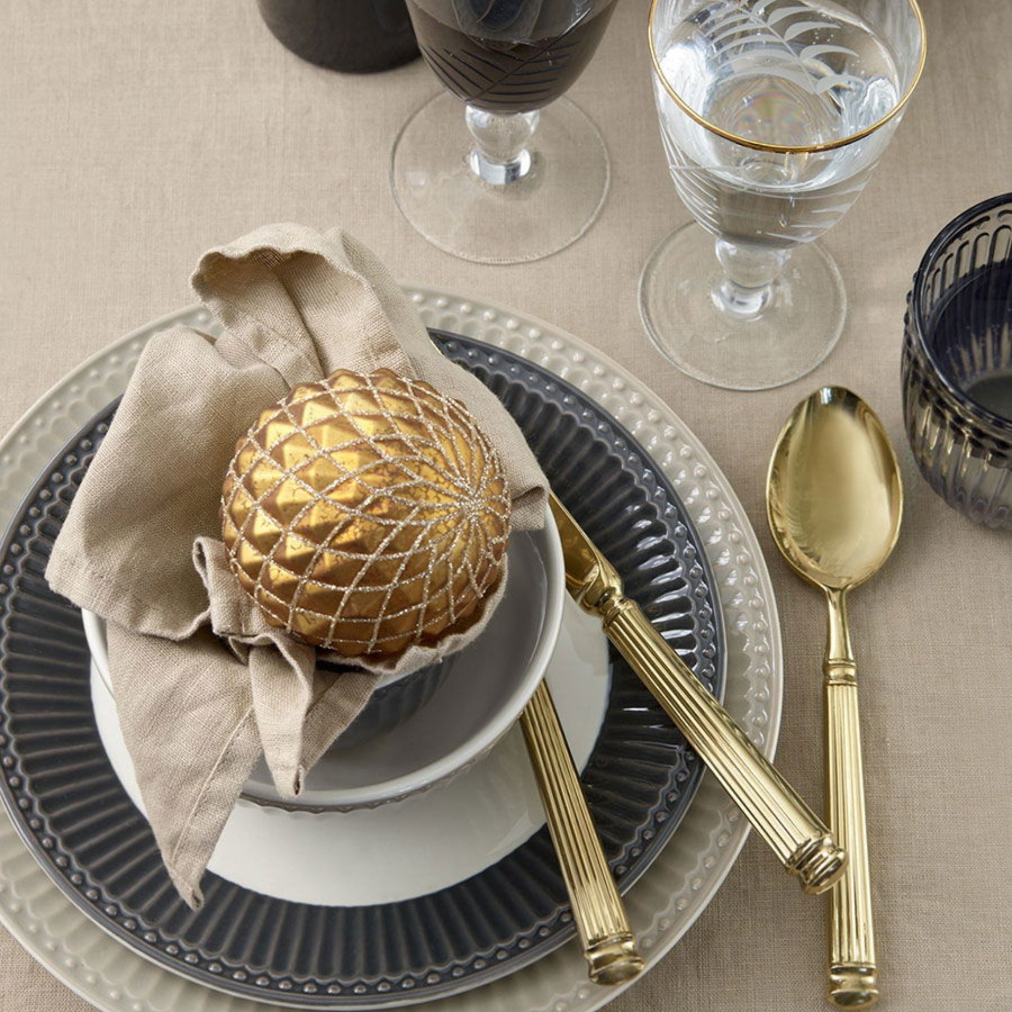 Goldbesteck von GreenGate, bestehend aus Messer, Gabel und Löffel, stilvoll auf einem Esstisch arrangiert.