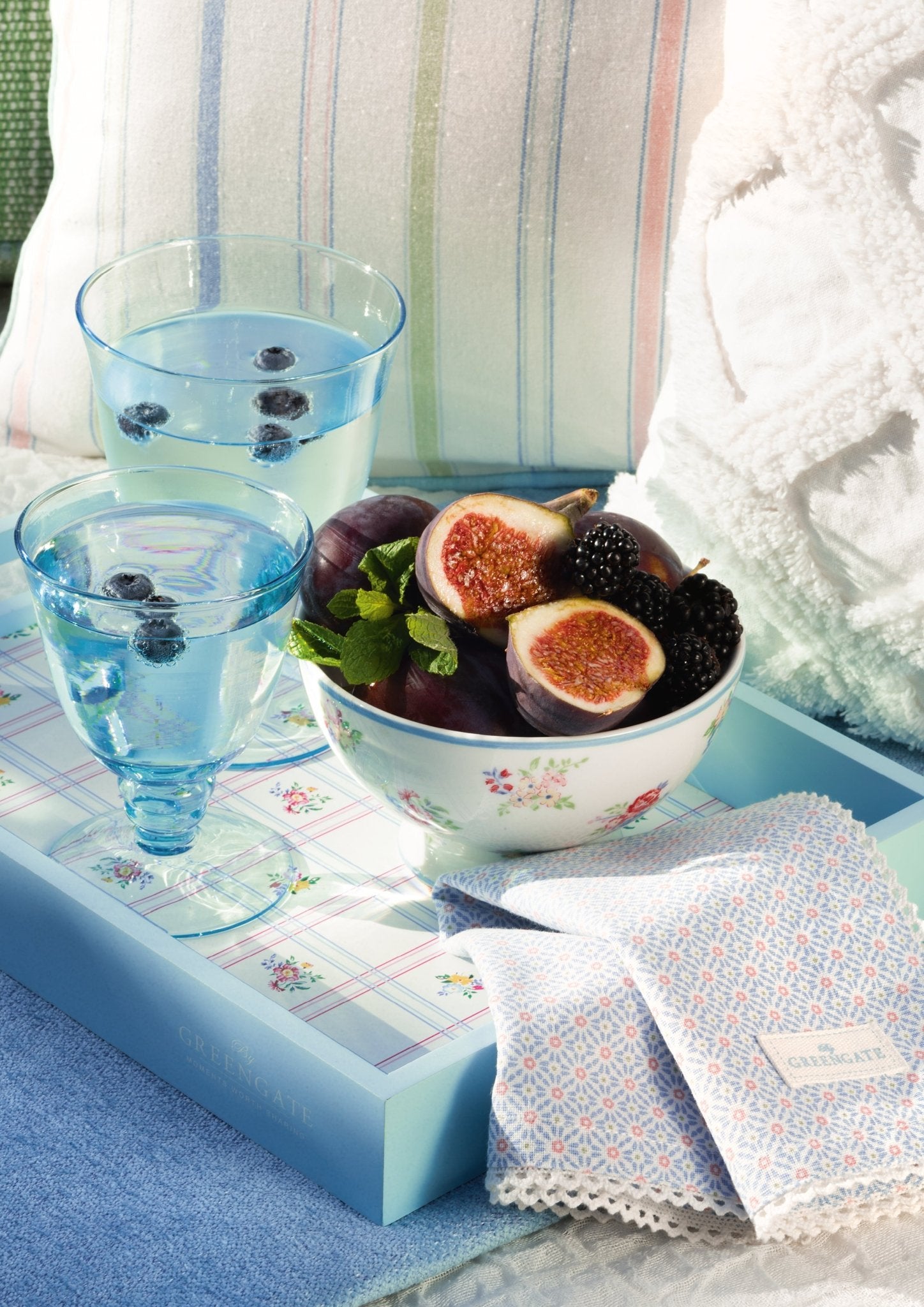 Weingläser GreenGate in hellblau mit Wasser und Blaubeeren, auf einem sommerlichen hellblauen Tablett neben einer mit Obst gefüllten Obstschale
