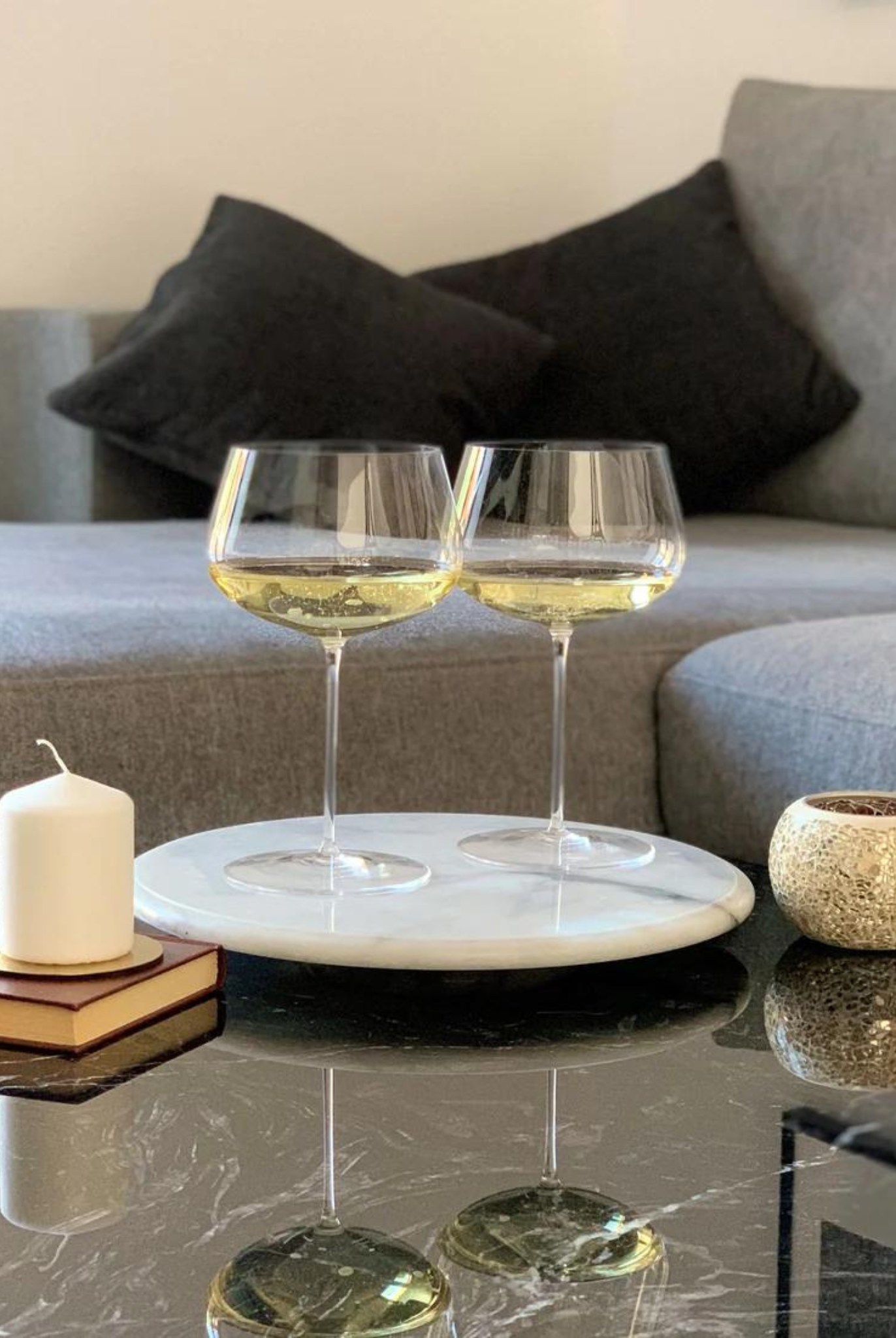 Zwei Weißweingläser transparent mit Weißwein gefüllt auf Couchtisch im Wohnzimmer stehend