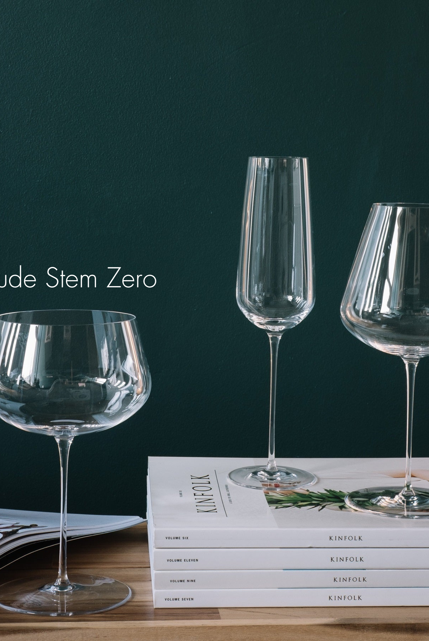 Weißweinglas transparent auf Holzplatte stehend neben Stapel Zeitschriften weiß auf den ein Champagnerglas transparent und Rotweinglas transparent stehen