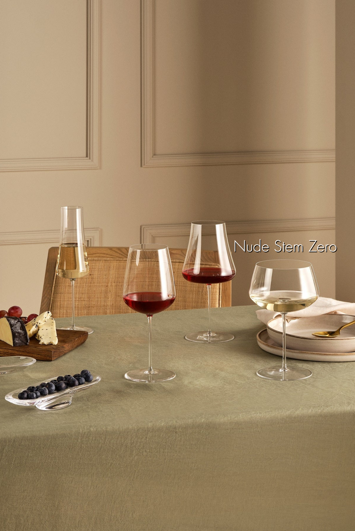 Weißweinglas transparent mit Weißwein gefüllt auf gedecktem Esstisch stehend neben zwei transparenten gefüllten Rotweingläsern und einem gefüllten Champagnerglas