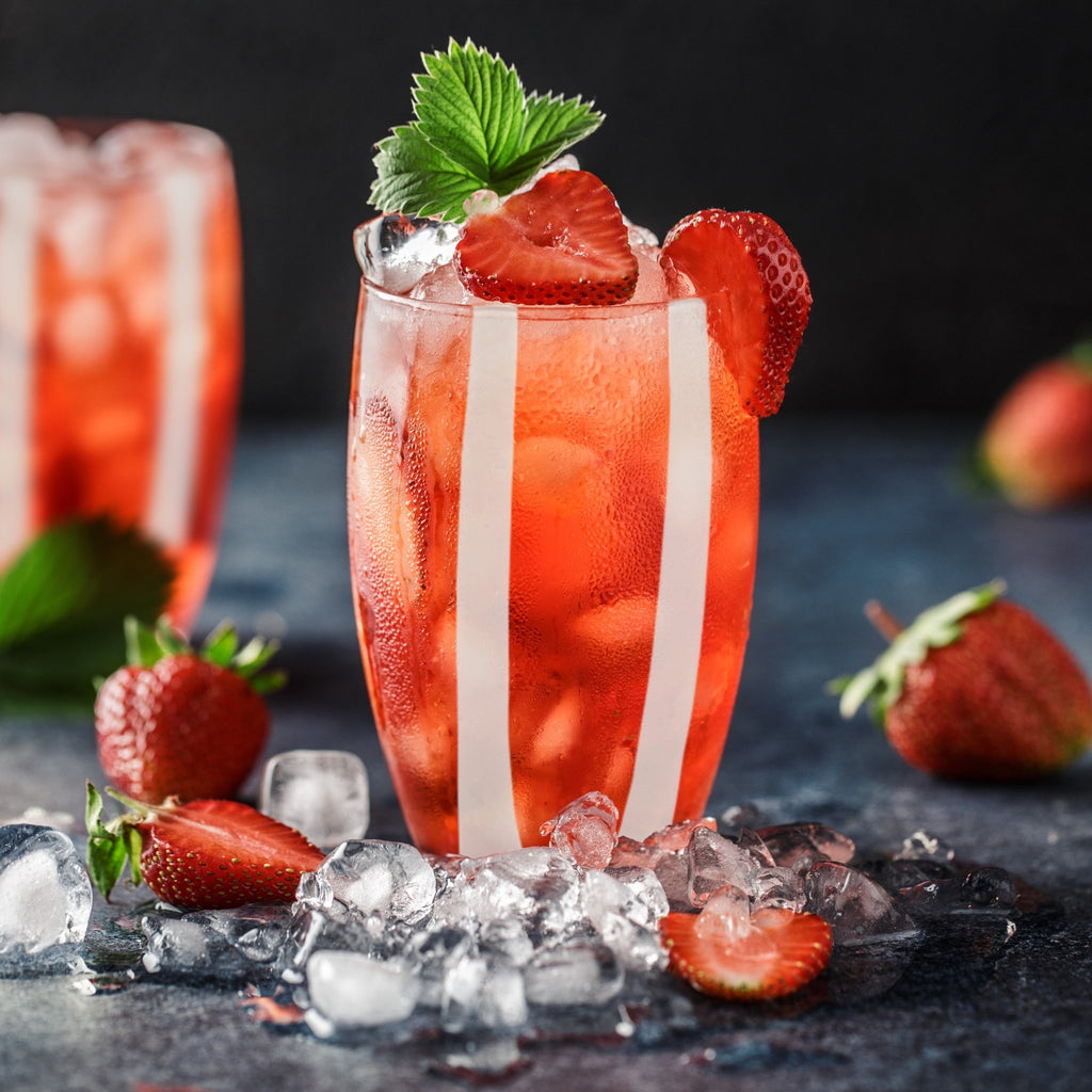 Trinkglas Farbe rot mit weißen Streifen, dekoriert mit Eiswürfeln, Erdbeeren und Zimtblättern im Trinkglas und um das Glas herum