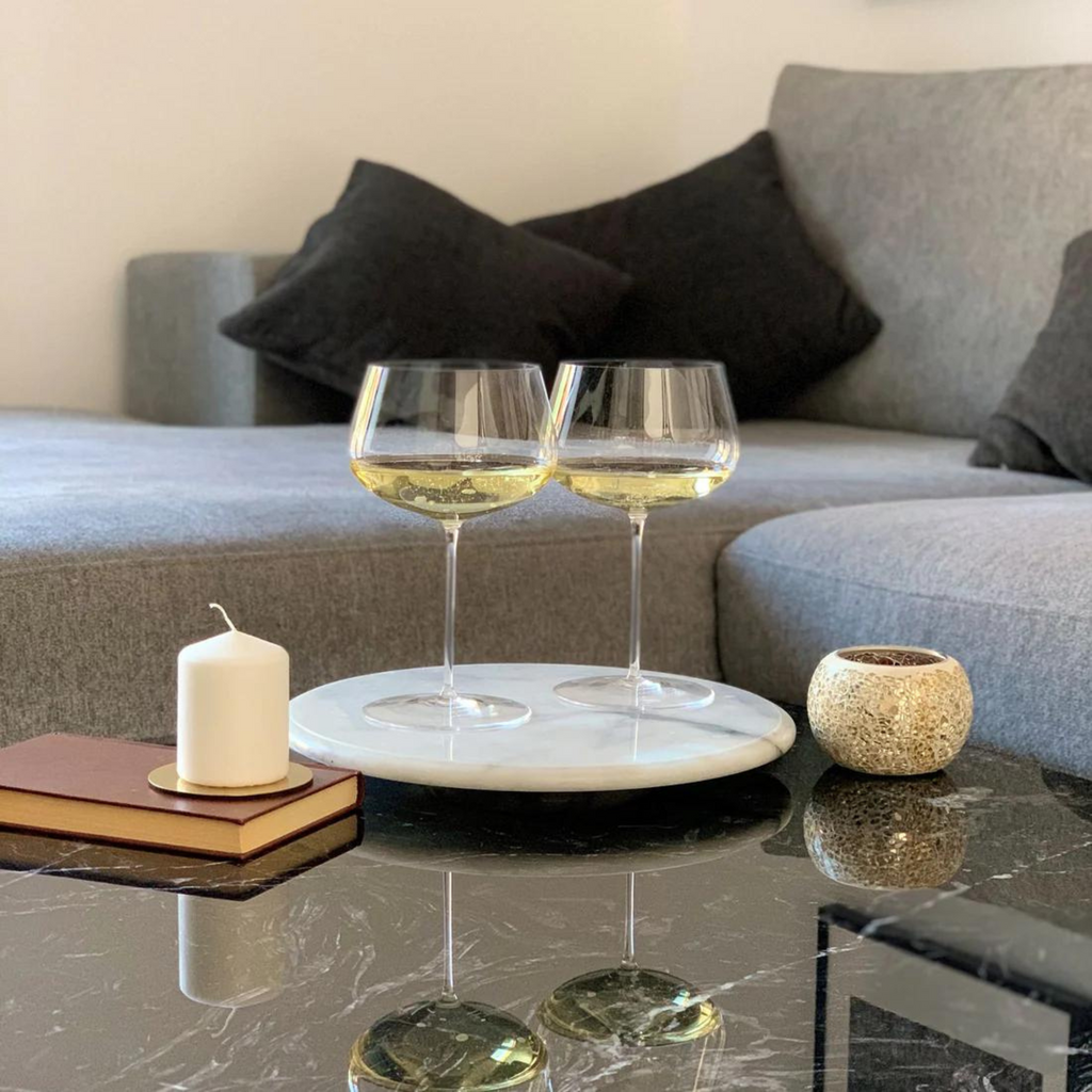 Zwei Weißweingläser transparent mit Weißwein gefüllt auf Couchtisch im Wohnzimmer stehend