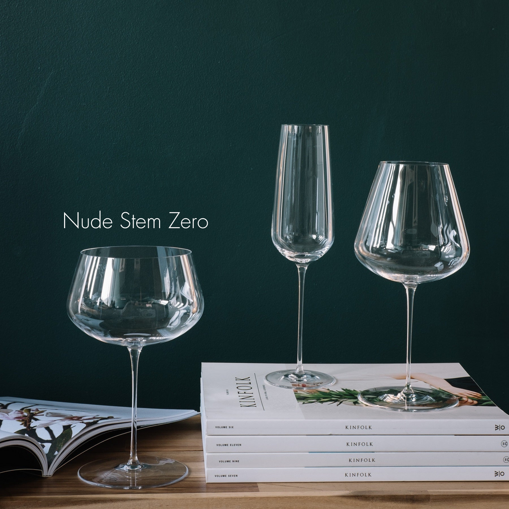 Weißweinglas transparent auf Holzplatte stehend neben Stapel Zeitschriften weiß auf den ein Champagnerglas transparent und Rotweinglas transparent stehen