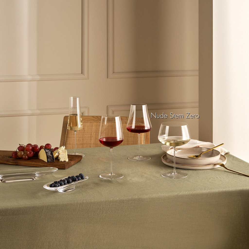 Weißweinglas transparent mit Weißwein gefüllt auf gedecktem Esstisch stehend neben zwei transparenten gefüllten Rotweingläsern und einem gefüllten Champagnerglas