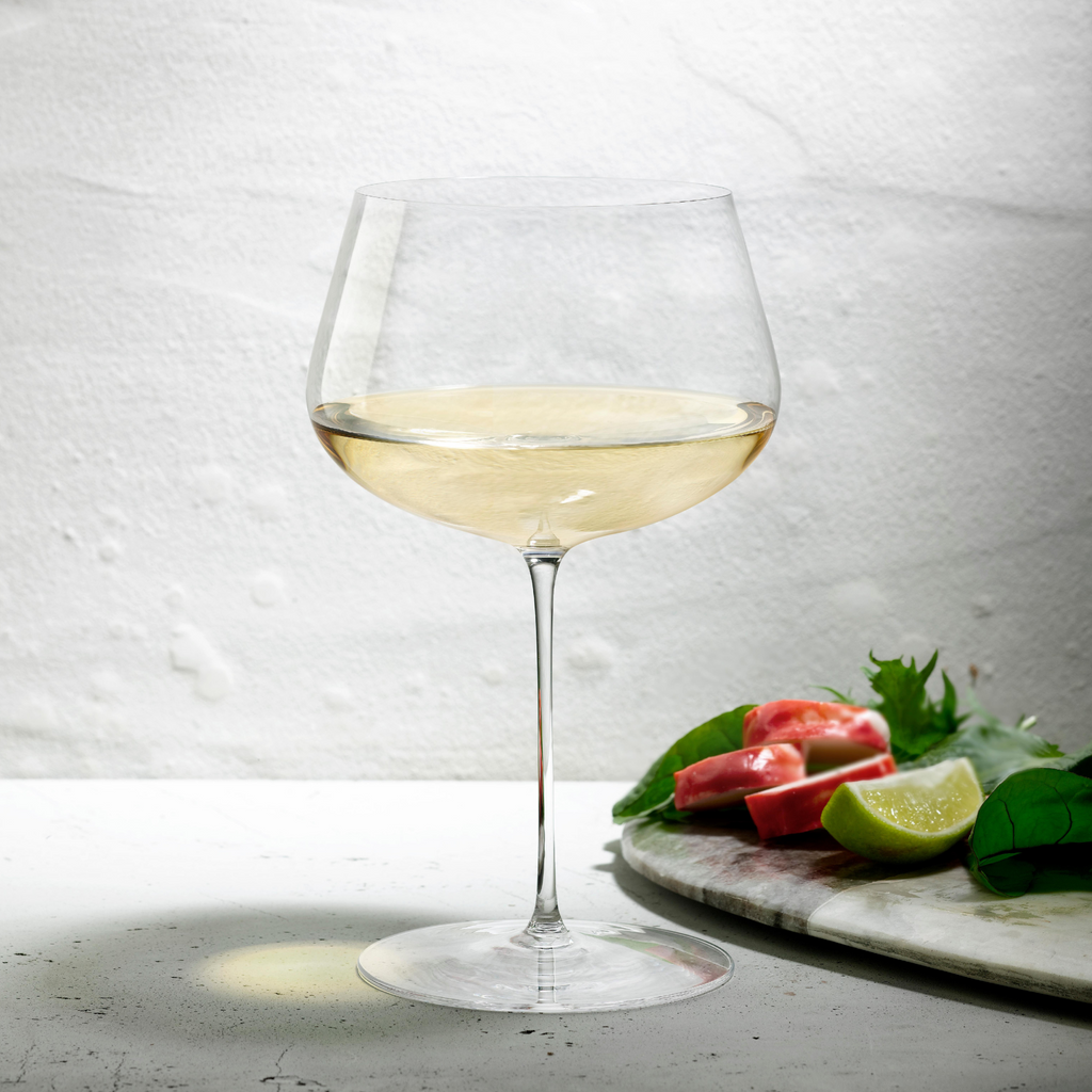 Weißweinglas transparent mit Weißwein gefüllt auf Tisch stehend neben Brett mit geschnittenen Früchten
